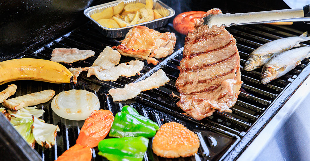 Steak meat, fish, and vegetables cooking on a grill.