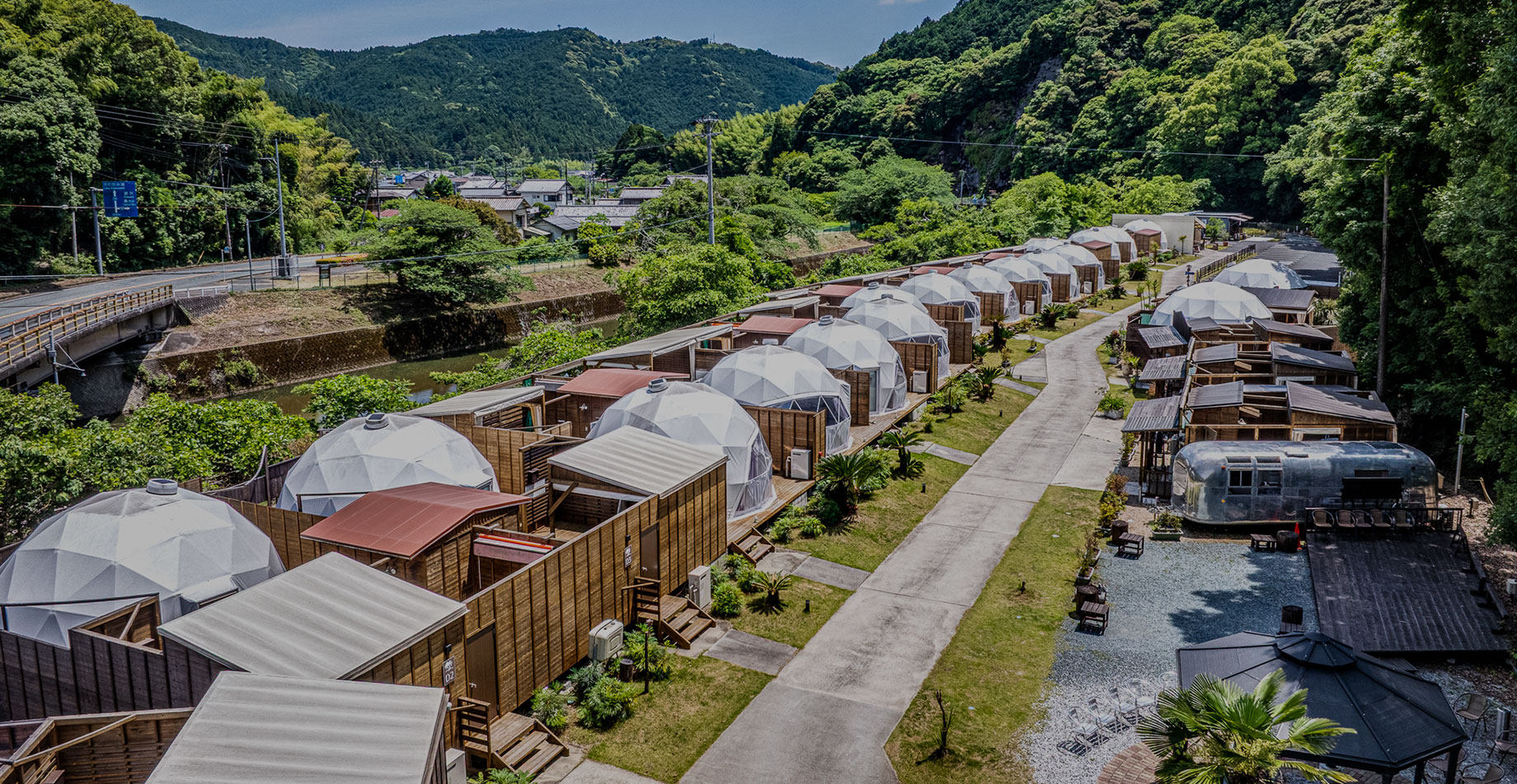 Bird’s-eye view of glamping dome tents lined up in a lush green valley.