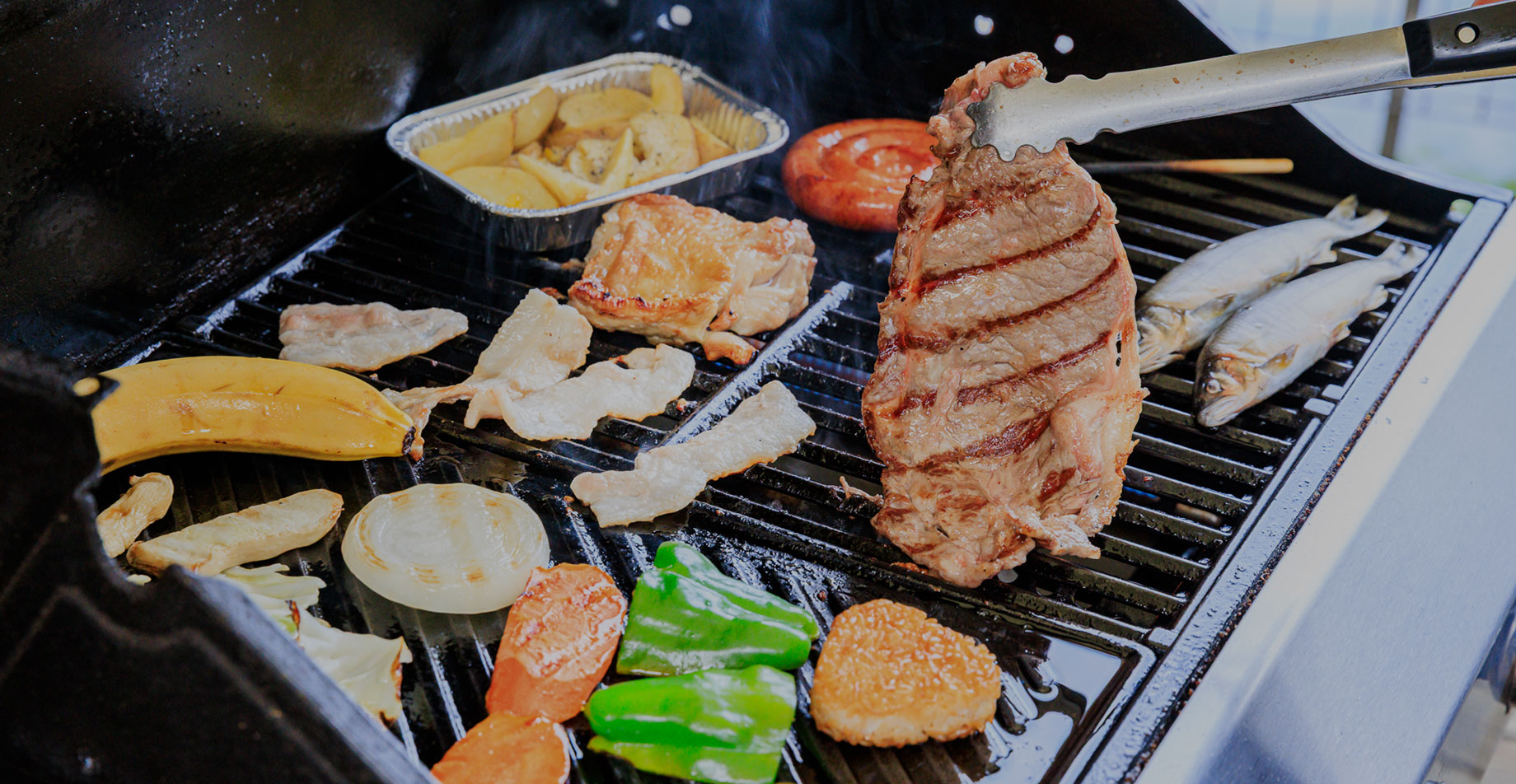 Cooking steak meat and other ingredients on a grill using tongs.