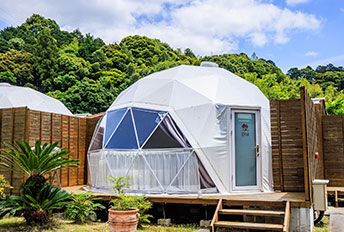 Exterior of a white glamping dome tent under a blue sky.