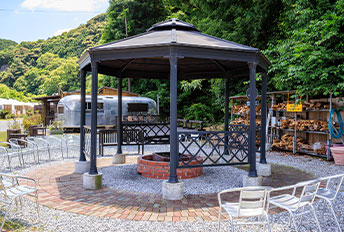 A large black gazebo with white chairs arranged around it in a lush green outdoor area.