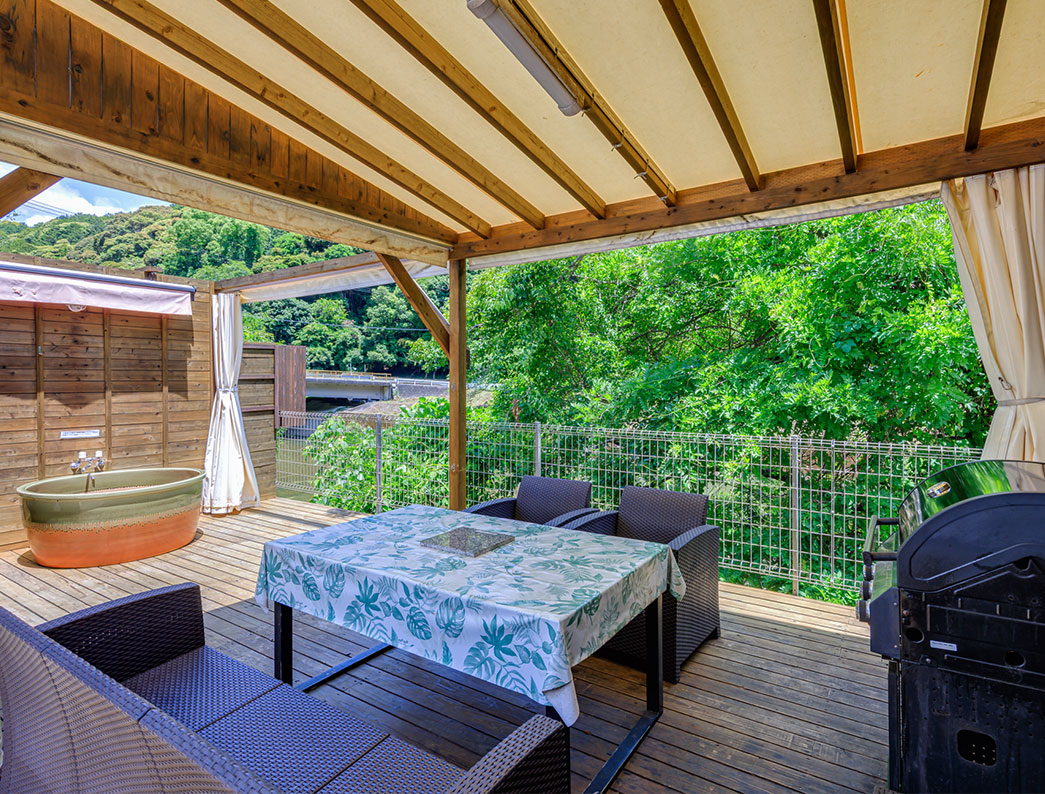 The wooden deck is equipped with table seating and a BBQ grill, and an outdoor bathtub is located in the far left corner.