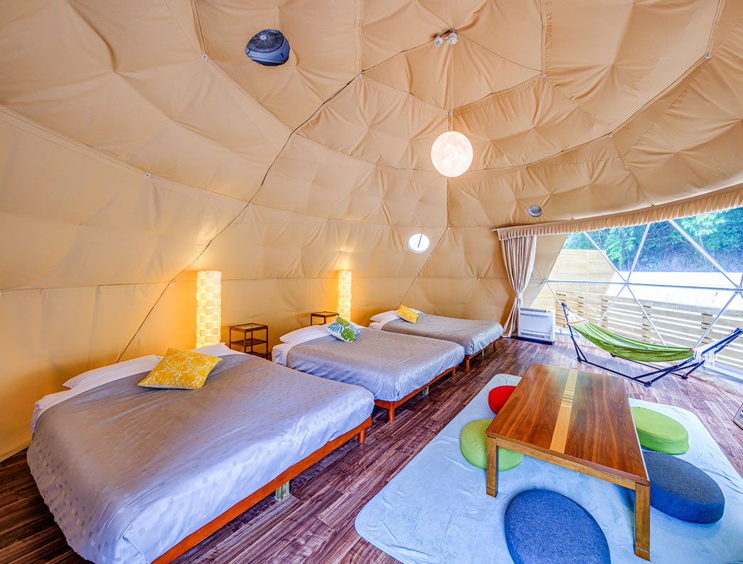 Nighttime view inside a dome tent furnished with beds, a low table, and floor cushions.