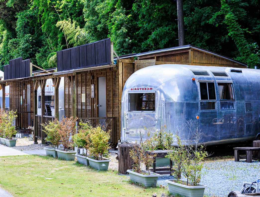 Silver Airstream-style trailer house parked in a lush outdoor setting.